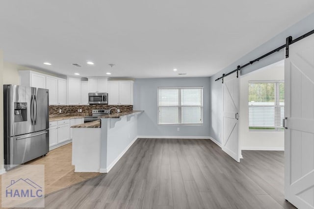 kitchen featuring kitchen peninsula, light wood-type flooring, stainless steel appliances, a barn door, and white cabinets