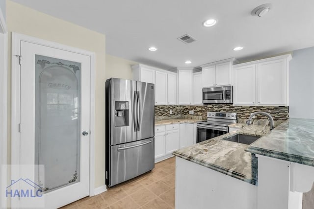 kitchen with light stone counters, kitchen peninsula, decorative backsplash, white cabinets, and appliances with stainless steel finishes