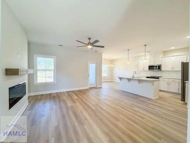 kitchen with white cabinetry, hanging light fixtures, appliances with stainless steel finishes, a kitchen breakfast bar, and an island with sink