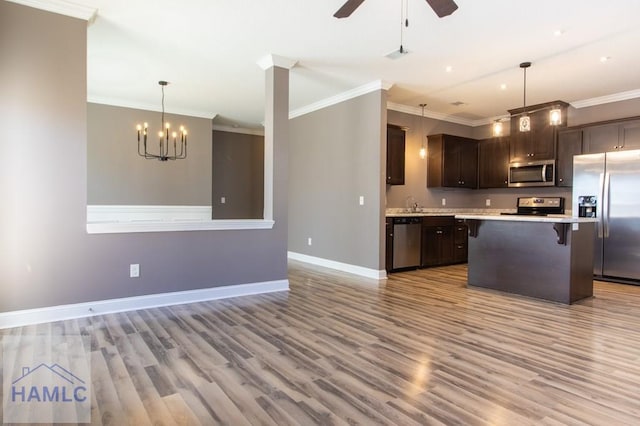 kitchen with light countertops, dark brown cabinets, appliances with stainless steel finishes, a kitchen bar, and ceiling fan with notable chandelier