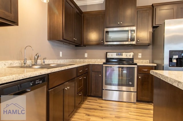 kitchen with dark brown cabinets, stainless steel appliances, light wood-type flooring, and a sink