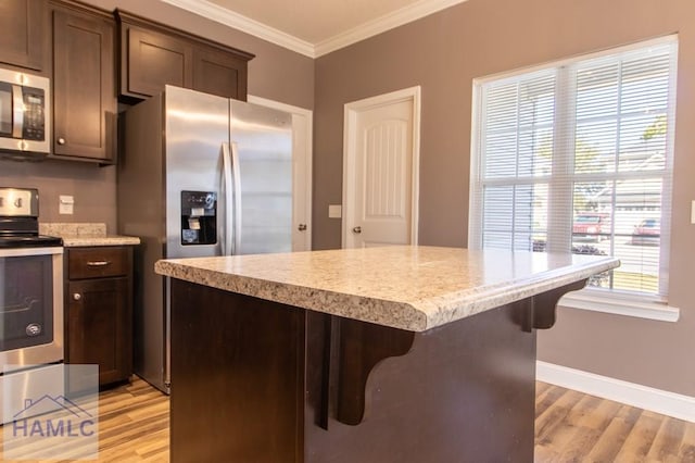 kitchen with a kitchen island, baseboards, light wood-type flooring, ornamental molding, and stainless steel appliances