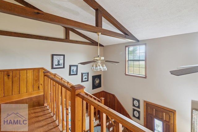 staircase with ceiling fan, vaulted ceiling with beams, and a textured ceiling