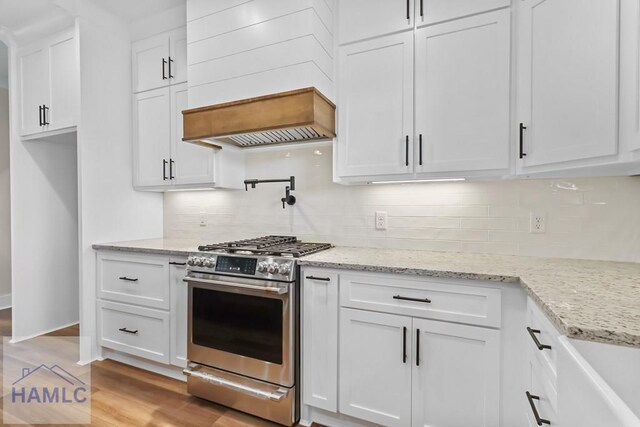 kitchen featuring stainless steel range with gas stovetop, tasteful backsplash, white cabinetry, custom range hood, and light stone countertops