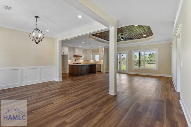 unfurnished living room with crown molding, a tray ceiling, baseboards, dark wood-type flooring, and visible vents