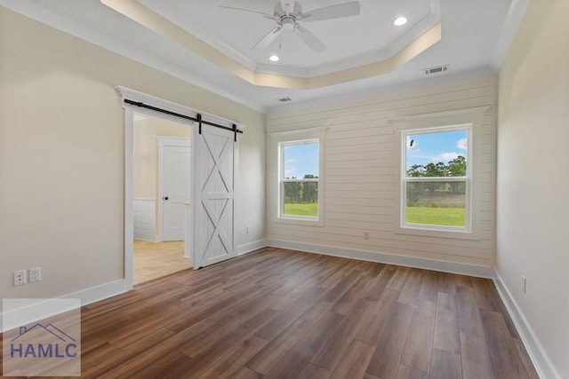 unfurnished bedroom with a barn door, wood finished floors, multiple windows, and a raised ceiling
