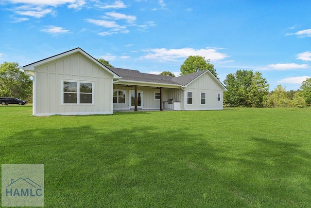 rear view of property with board and batten siding, a ceiling fan, and a yard