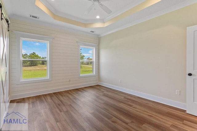 unfurnished room featuring a barn door, wood finished floors, a raised ceiling, baseboards, and visible vents