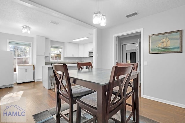 dining space featuring hardwood / wood-style flooring, a notable chandelier, sink, and a textured ceiling