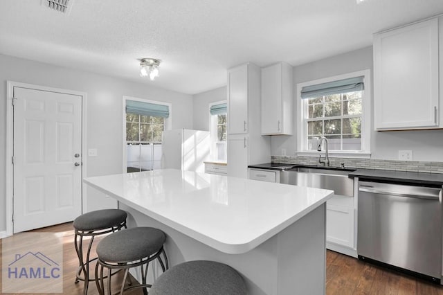 kitchen with sink, a kitchen island, stainless steel dishwasher, dark hardwood / wood-style floors, and white cabinets