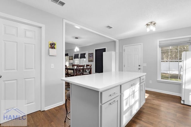 kitchen with dark wood-type flooring, white fridge, decorative light fixtures, a breakfast bar area, and a kitchen island