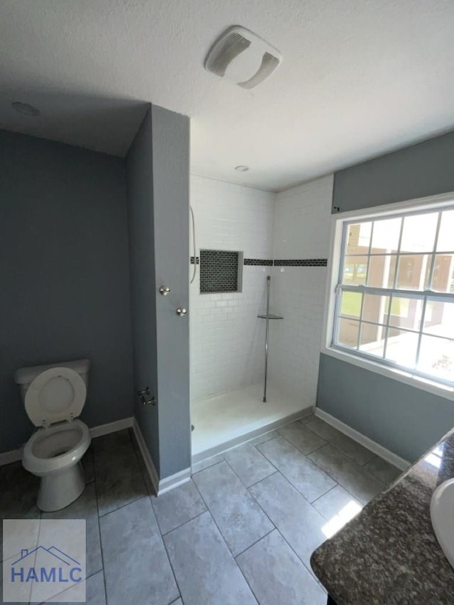 bathroom featuring a tile shower, tile patterned floors, a textured ceiling, toilet, and vanity