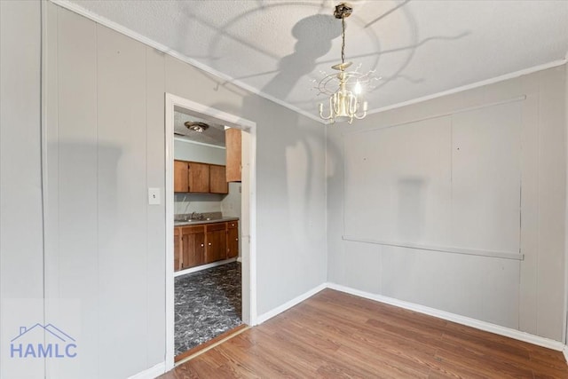 unfurnished dining area featuring sink, hardwood / wood-style floors, crown molding, and a chandelier