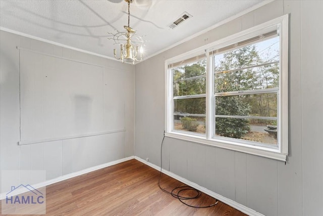 unfurnished room with plenty of natural light, hardwood / wood-style floors, crown molding, and a notable chandelier