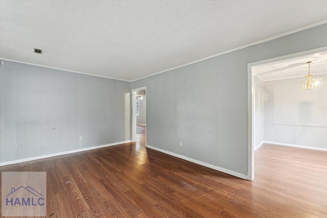 unfurnished room with hardwood / wood-style floors, a textured ceiling, a notable chandelier, and ornamental molding