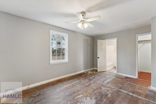 unfurnished bedroom featuring ceiling fan, dark hardwood / wood-style flooring, ensuite bath, a walk in closet, and a closet