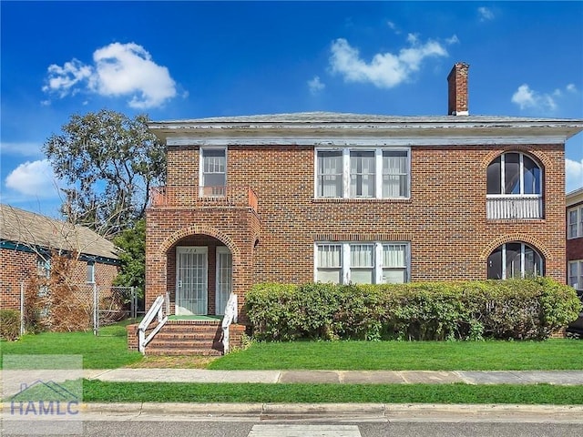 view of front facade with brick siding, a chimney, and a front lawn