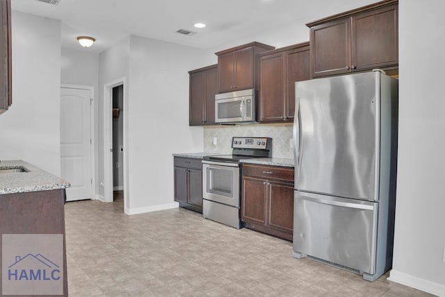 kitchen with dark brown cabinets, light stone countertops, and appliances with stainless steel finishes