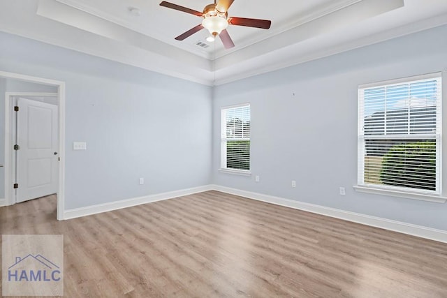 empty room with a tray ceiling, baseboards, and light wood-style floors