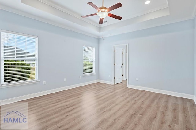 empty room featuring a tray ceiling, light wood-style floors, and baseboards