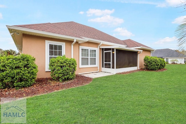 back of house with a yard, a shingled roof, stucco siding, and a sunroom