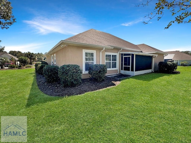 rear view of property featuring a shingled roof, a yard, a sunroom, and stucco siding