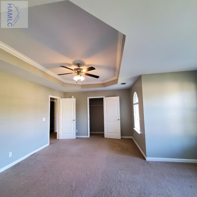 unfurnished bedroom with carpet, a walk in closet, a tray ceiling, ceiling fan, and crown molding