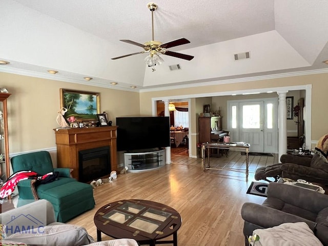 living room featuring ornate columns, ceiling fan, light wood-type flooring, a tray ceiling, and ornamental molding