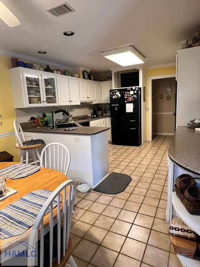 kitchen with black fridge, crown molding, sink, light tile patterned floors, and white cabinets