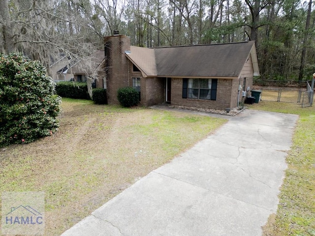 single story home featuring brick siding, fence, driveway, a chimney, and a front yard