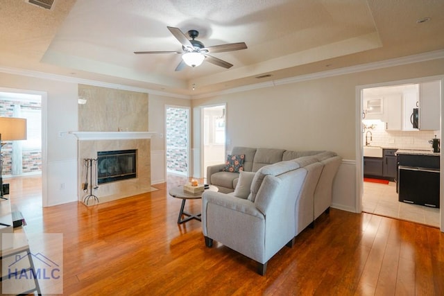 living room featuring a wealth of natural light, a raised ceiling, ceiling fan, and wood-type flooring