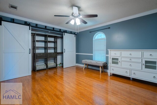 bedroom with crown molding, visible vents, wood finished floors, and a barn door