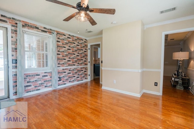 empty room with crown molding, ceiling fan, wood finished floors, and brick wall