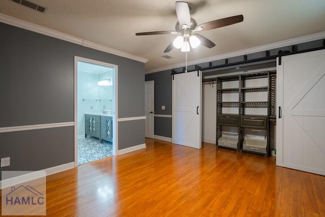 unfurnished bedroom featuring wood finished floors, a barn door, crown molding, and visible vents