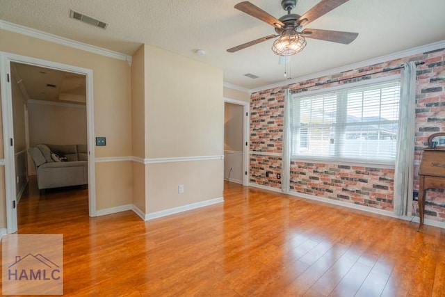 spare room with a ceiling fan, visible vents, light wood-style flooring, and brick wall