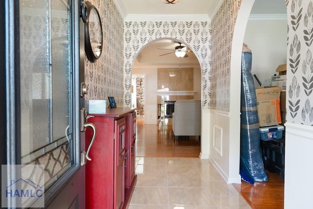 foyer featuring ceiling fan, wallpapered walls, arched walkways, ornamental molding, and wainscoting