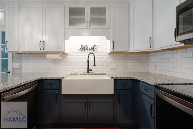 kitchen featuring decorative backsplash, white cabinets, a sink, appliances with stainless steel finishes, and light stone countertops