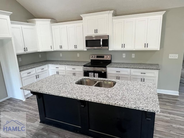 556 Caleb Cir, Jesup, GA 31545 - kitchen featuring stainless steel appliances, white cabinets, a center island with sink, light stone countertops, and vaulted ceiling
