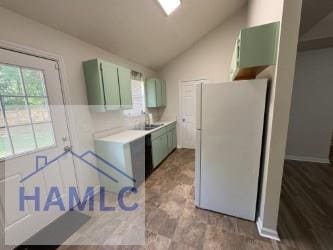 kitchen with a sink, light countertops, freestanding refrigerator, vaulted ceiling, and green cabinets