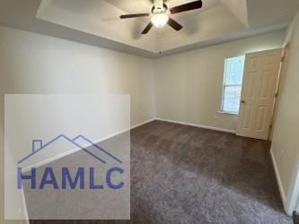 carpeted empty room with a ceiling fan, baseboards, and a raised ceiling