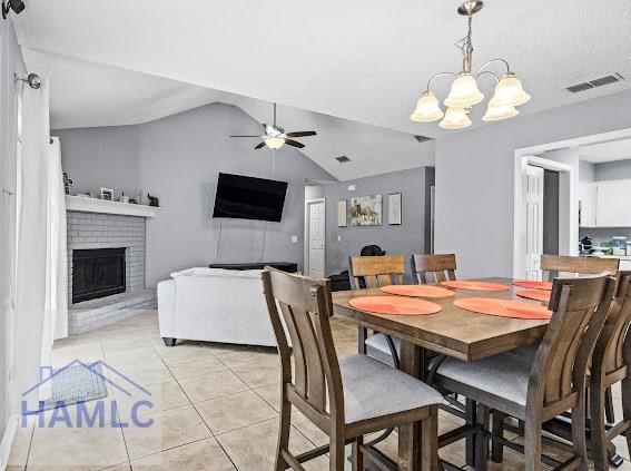 tiled dining room featuring lofted ceiling, ceiling fan with notable chandelier, and a fireplace