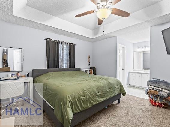 carpeted bedroom featuring ceiling fan, a tray ceiling, ensuite bath, and a textured ceiling