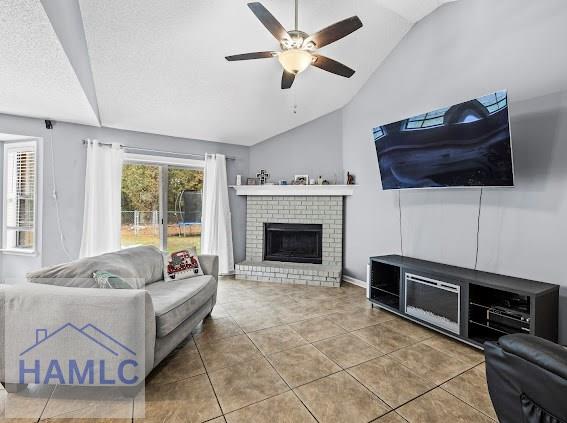 tiled living room featuring lofted ceiling, a textured ceiling, ceiling fan, and a brick fireplace