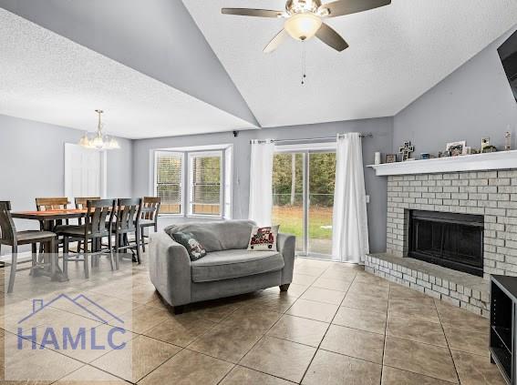 living room featuring ceiling fan with notable chandelier, a fireplace, lofted ceiling, tile patterned flooring, and a textured ceiling