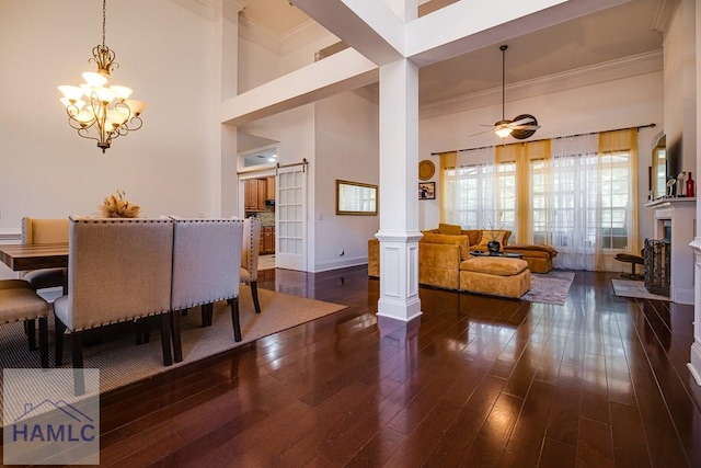 dining room featuring ornate columns, dark wood-type flooring, a barn door, crown molding, and ceiling fan with notable chandelier