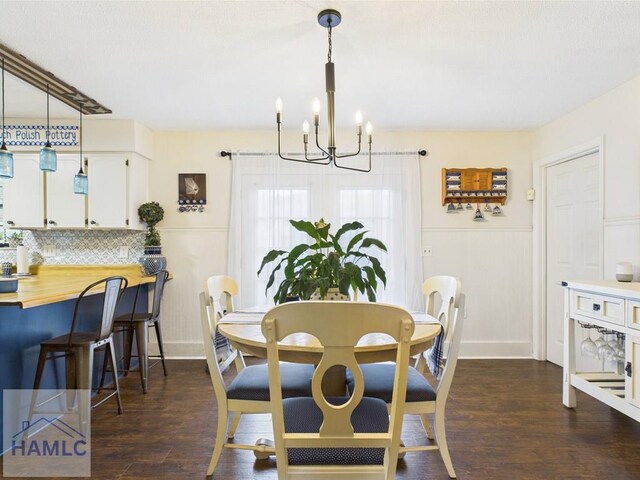 dining room with a chandelier, dark wood finished floors, a wainscoted wall, and a decorative wall