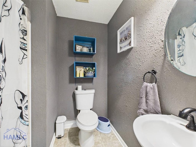full bath featuring a sink, toilet, a shower with curtain, tile patterned floors, and a textured ceiling