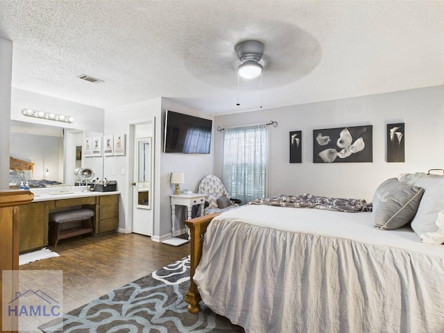 bedroom with dark wood-type flooring, a textured ceiling, ensuite bathroom, and ceiling fan