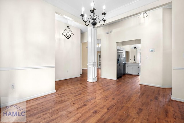 unfurnished dining area with baseboards, dark wood finished floors, a notable chandelier, a high ceiling, and a sink