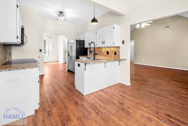 kitchen featuring light stone counters, a peninsula, a sink, white cabinetry, and dark wood-style floors